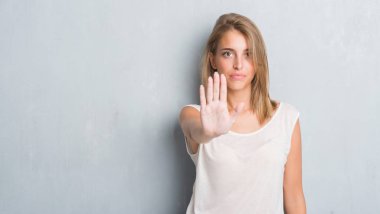 Açık eliyle dur işareti ile ciddi ve kendine güvenen ifade, savunma jest yapıyor grunge gri duvar üzerinde duran güzel genç kadın