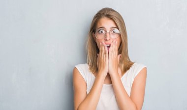 Grunge gri duvar giyen gözlük kapak ağız elle hata, korku, sessizlik içinde gizli kavramı korkmuş ifade için utanç ile şok üzerinde duran güzel genç kadın