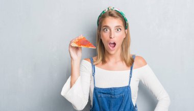 Pepperoni pizza dilimi bir sürpriz yüz, korkuyor ve heyecanlı korku ifadesi ile şok korkmuş yeme grunge gri duvar güzel genç kadın