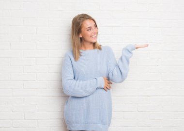 Beyaz tuğla duvar neşeli sunulması ve kameraya bakarak avucunun ile işaret gülümseyen güzel genç kadın.