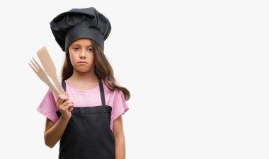 Brunette hispanic girl wearing cook uniform with a confident expression on smart face thinking serious clipart