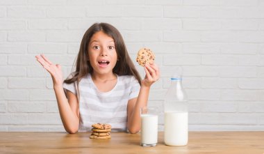Süt içme ve büyük gülümseme ile çığlık zaferini kutluyor ve ellerini kaldırdı çikolata bisküvi çok mutlu ve heyecanlı, kazanan ifade yemek masada oturan genç İspanyol çocuk