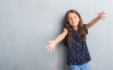 Sarılmak için kollarını açarak gülümseyerek kameraya bakarak grunge gri duvar genç İspanyol çocuk. Neşeli ifade kucaklayan mutluluk.