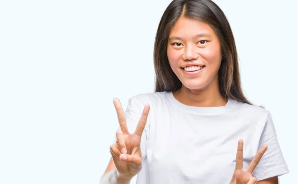 年轻的亚洲妇女在孤立的背景下微笑着看着相机 显示手指做胜利的标志 第二个 — 图库照片