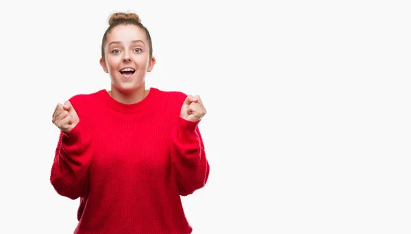 パンと赤いセーターを祝うを身に着けている若いブロンドの女性驚いて腕を上げると成功のため驚くし 目を開きます 勝者の概念 — ストック写真