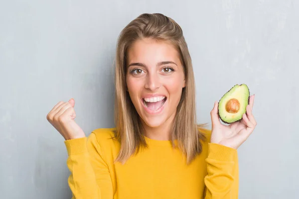 Hermosa Mujer Joven Sobre Pared Gris Grunge Comiendo Aguacate Gritando —  Fotos de Stock