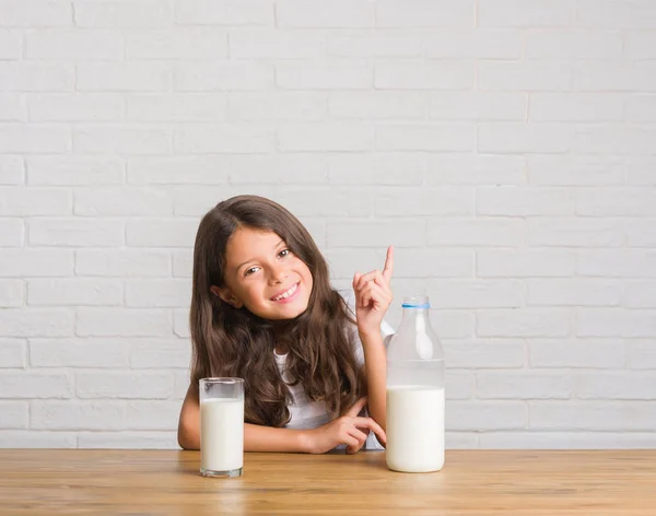 側の手と指で指す非常にハッピー ミルクのガラスを飲むテーブルに座って若いヒスパニックの子供 — ストック写真