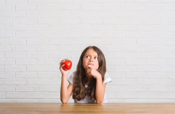 年轻的西班牙裔孩子坐在餐桌上吃新鲜的西红柿严肃的面孔思考问题 非常困惑的想法 — 图库照片