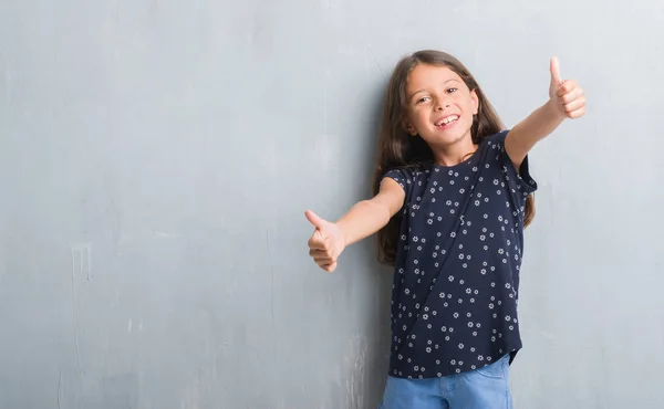 年轻的西班牙裔孩子在灰色墙壁上批准做积极的手势与手 竖起大拇指微笑 并为成功而高兴 看着相机 胜利者的手势 — 图库照片