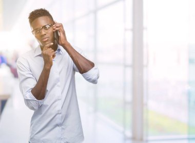 Smartphone ciddi bir yüz düşünme soru hakkında çok kullanan genç Afro-Amerikan adam fikir karışık