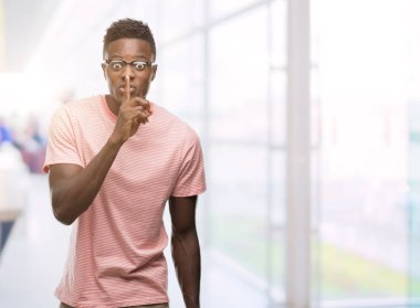 Dudaklarında parmak ile sessiz olmanı pembe t-shirt giyen genç Afro-Amerikan adam. Sessizlik ve gizli kavramı.