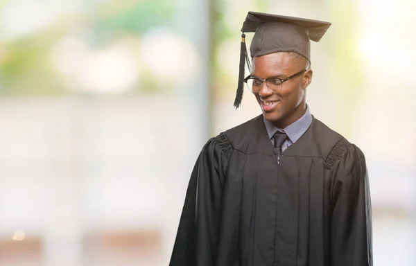 Young graduated african american man over isolated background looking away to side with smile on face, natural expression. Laughing confident.