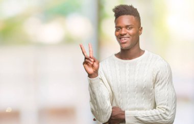 Afrikalı-Amerikalı genç mutlu yüz zafer işareti yaparken kameraya göz kırpıyor ile gülümseyen izole arka plan üzerinde. İki numaralı.