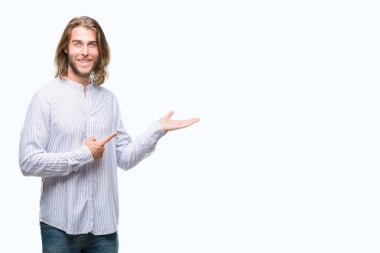 Hayret ve el ile sunulması ve parmak ile işaret ederken kameraya gülümseyen izole arka plan üzerinde uzun saçlı yakışıklı delikanlı.