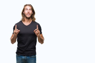 İzole arka plan üzerinde uzun saçlı yakışıklı delikanlı hayrete ve yukarıya bakıyor ve parmakları ile işaret ve silah kaldırdı şaşırttı.