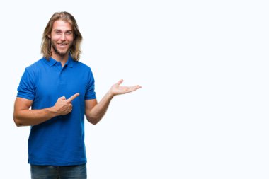 Hayret ve el ile sunulması ve parmak ile işaret ederken kameraya gülümseyen izole arka plan üzerinde uzun saçlı yakışıklı delikanlı.