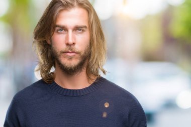 Genç yakışıklı adam uzun saçlı yüzünde ciddi bir ifade ile izole arka plan üzerinde kış kazak giyiyor. Basit ve doğal kameraya bakıyor.