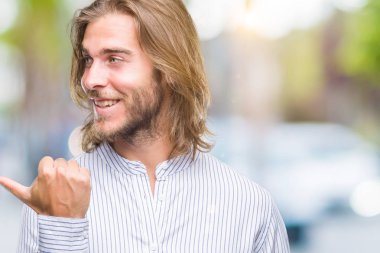 Seyir ve başparmak yanında yukarıyı mutlu yüz ile gülümseyen izole arka plan üzerinde uzun saçlı yakışıklı delikanlı.