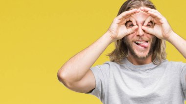 Yakışıklı delikanlı, dilini parmaklarının arasından baktığını yapışmasını dürbün gibi ok jest yapıyor izole arka plan üzerinde uzun saçlı. Deli ifade.