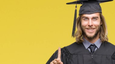 Genç yakışıklı adam uzun saçlı ve parmak gülümseyen süre bir numara ile kendinden emin ve mutlu yukarıyı gösteren izole arka plan üzerinde mezun oldu.