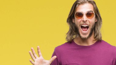 Üzerinde güneş gözlüğü takmış uzun saçlı yakışıklı delikanlı deli kutluyor arka plan izole ve silah ile başarı için yükseltilmiş ve açık gözleri heyecanlı çığlık hayrete düşürdü. Kazanan kavramı