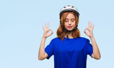 Genç güzel kadın giyiyor bisikletçi kask izole arka plan üzerinde dinlenmek ve gülümseyen gözlerle kapalı parmak jestle meditasyon yapıyor. Yoga kavramı.