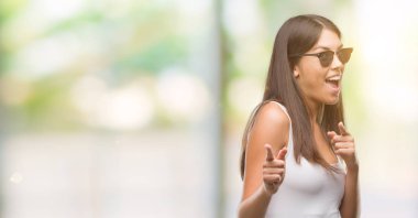 Genç güzel İspanyol fotoğraf makinesi ile mutlu ve komik yüz için parmakları işaret güneş gözlüğü takıyor. İyi enerji ve vibes.