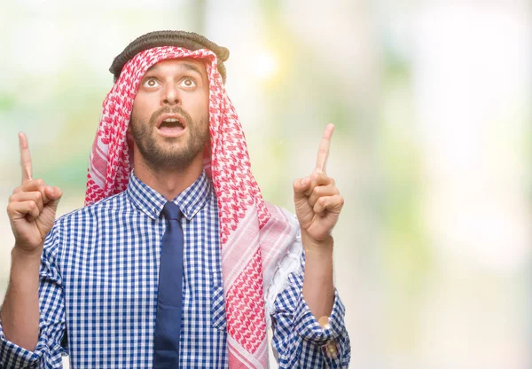 若いハンサムなアラビアン ビジネス人孤立の背景の上身に着けているクーフィーヤびっくり驚いて見上げると指で指していると腕を上げた — ストック写真
