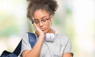 Kulaklıklar ve sırt çantası düşünme izole arka plan bakmaktan giyen genç afro Amerikan öğrenci kadın yorgun ve sıkılmış çapraz silah depresyon sorunları ile.