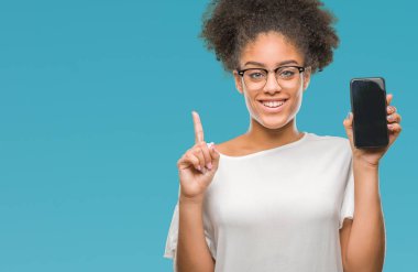 Genç güzel afro Amerikan gösteren smartphone izole arka bir fikirle sürpriz üzerinde ekran ya da gülen yüz, bir numara ile işaret parmağı soru