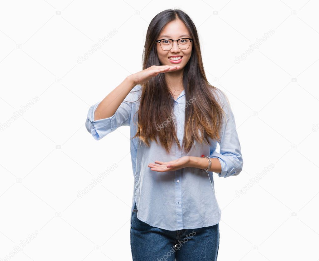 Young asian business woman wearing glasses over isolated background gesturing with hands showing big and large size sign, measure symbol. Smiling looking at the camera. Measuring concept.