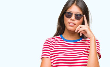 Genç Asyalı kadın elle çene düşünme hakkında soru, dalgın ifade izole arka plan üzerinde güneş gözlüğü takıyor. Düşünceli yüzüyle gülümsüyor. Şüphe kavramı.