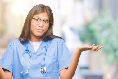 Genç Asyalı doktor kadın izole arka plan clueless ve şaşkın bir ifadeyle kollar ve eller kaldırdı. Şüphe kavramı.