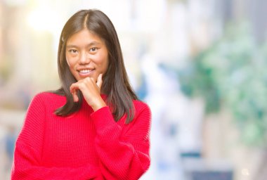 Emin çapraz kollar ve çeneme kaldırdı el ile gülümseme ile kameraya bakarak izole arka plan üzerinde kış kazak giyen genç Asyalı kadın. Pozitif düşünce.