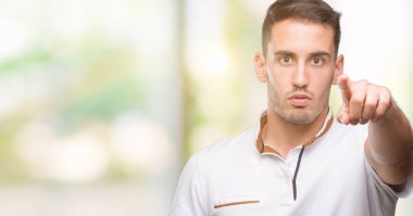 Yakışıklı genç casual adam beyaz t-shirt ile kamera ve size, el işareti, pozitif ve kendinden emin bir jest ön parmakla giyiyor