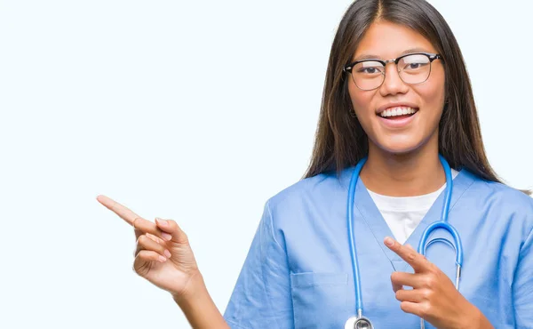笑顔で側に つの手と指で指しているカメラを見て孤立の背景の上の若いアジア医師女性 — ストック写真