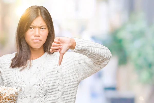 年轻的亚洲妇女吃爆米花在孤立的背景与愤怒的脸 消极的迹象显示不喜欢拇指向下 拒绝概念 — 图库照片