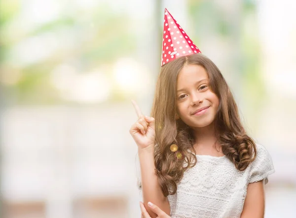 側の手と指で指す非常に幸せな誕生日の帽子を身に着けているヒスパニックのブルネットの少女 — ストック写真