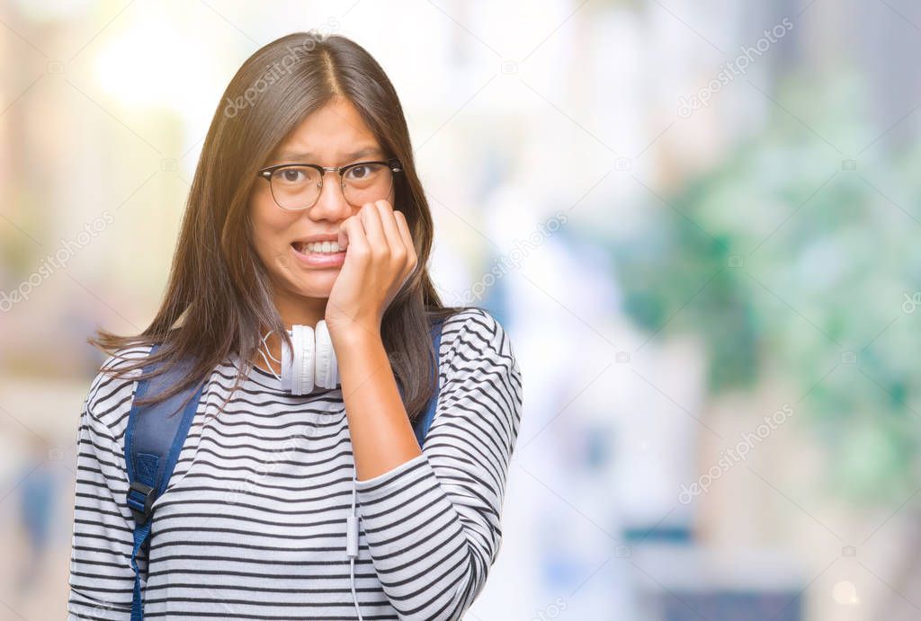 Young asian student woman wearing headphones and backpack over isolated background looking stressed and nervous with hands on mouth biting nails. Anxiety problem.