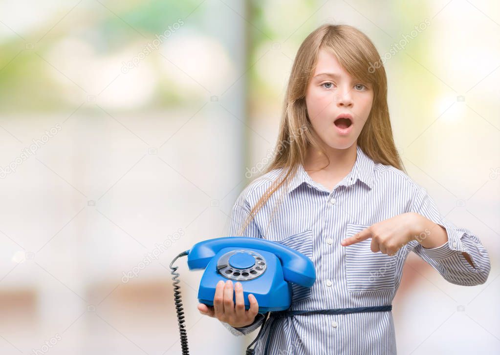 Young blonde toddler holding vintage telephone very happy pointing with hand and finger