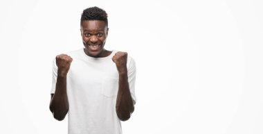 Beyaz kutluyor t-shirt giyen genç Afro-Amerikan adam şaşırttı ve başarı için kaldırdı kollarını açarak hayret ve gözleri açık. Kazanan kavramı.