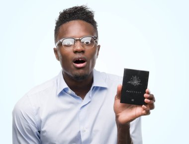 Genç Afro-Amerikan adam holding Avustralya pasaportu bir sürpriz yüz, korkuyor ve heyecanlı korku ifadesi ile şok korkmuş