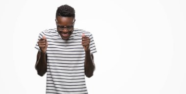 Gözlük ve lacivert t-shirt silah ile başarı için heyecanlı giyen genç Afro-Amerikan adam zafer kutluyor gülümseyen kaldırdı. Kazanan kavramı.