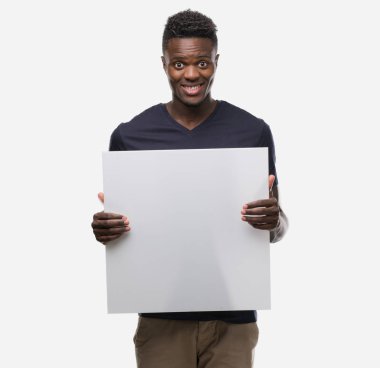 Genç Afro-Amerikan adam ayakta ve diş gösterilen kendine güvenen bir gülümsemeyle gülümseyerek mutlu bir yüz ile bir afiş tutarak