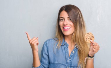 Çikolatalı bisküvi el ve parmak ile tarafına işaret çok mutlu yemek gri grunge duvarın üzerinden Genç Yetişkin kadın