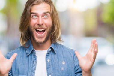 Yakışıklı delikanlı deli kutluyor ve silah ile başarı için heyecanlı çığlık kaldırdı ve açık gözleri hayret izole arka plan üzerinde uzun saçlı. Kazanan kavramı