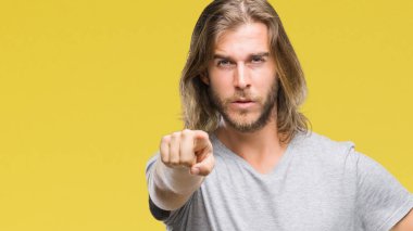 Young handsome man with long hair over isolated background holding football ball pointing with finger to the camera and to you, hand sign, positive and confident gesture from the front clipart