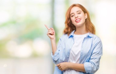 Kameraya bakarak yan el ve parmak ile işaret eden genç güzel iş kadını yüzünde kocaman bir gülümseme ile izole arka plan üzerinde.