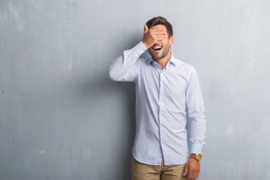 Şık gömlek gülümseyen ve gözler için sürpriz kapsayan yüz el ile gülüyor gri grunge duvarın üzerinden yakışıklı genç iş adamı. Kör kavramı.