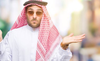 Keffiyeh izole arka plan clueless ve şaşkın bir ifadeyle kollar ve eller kaldırdı üzerinde giyen genç yakışıklı adam. Şüphe kavramı.